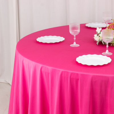 Pink tablecloth draped over a round table with white plates and glassware.