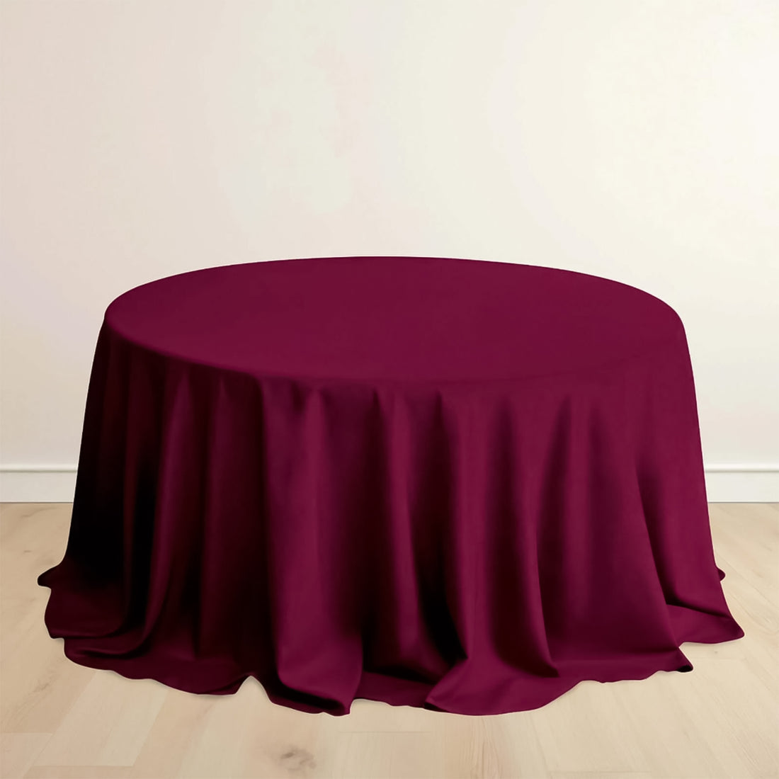 Burgundy round tablecloth draped over a table on a light wooden floor.