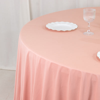 Pink round tablecloth draped over a table with white plates and a glass.