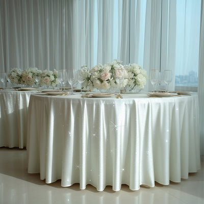 Elegant white table setting with floral arrangements and sparkling tablecloth.
