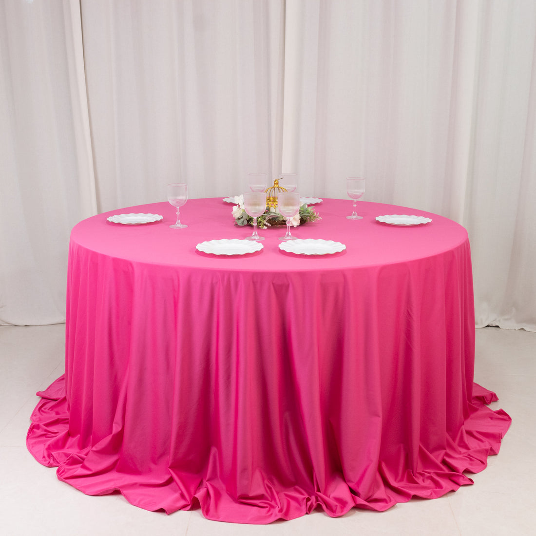 Pink round tablecloth draped elegantly over a table with plates and glasses on top.