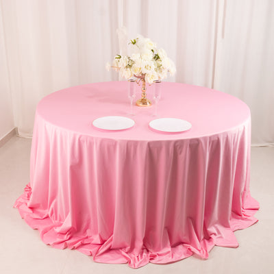 Round pink tablecloth with elegant white plates and a floral centerpiece.