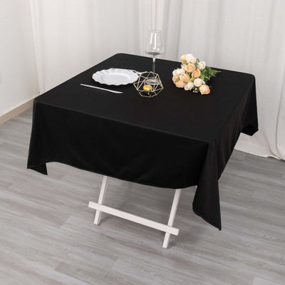 Black tablecloth on a dining table set with a glass, plate, and flowers.