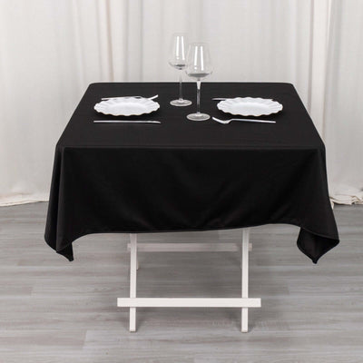 Black tablecloth draped over a folding table set with plates and glasses.