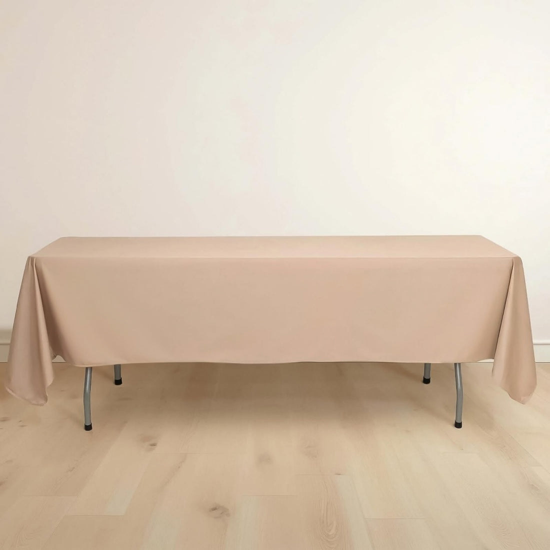 Beige tablecloth draped over a folding table on a light wooden floor.