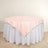 Round table with a pink tablecloth and white skirt on a light wooden floor.
