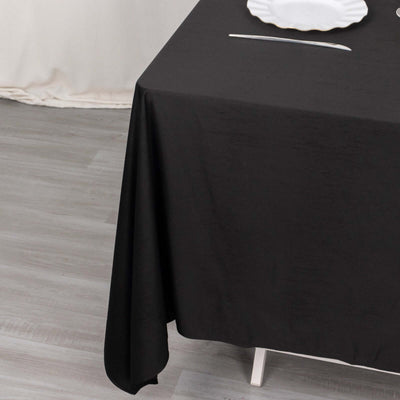 Black tablecloth draping over a table with a white plate on top.