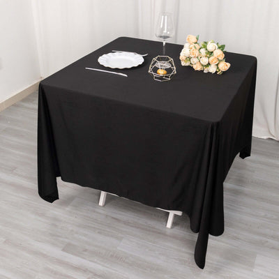 Black tablecloth draped over a table set for a meal with flowers and tableware.