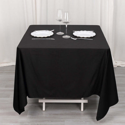 Black tablecloth with white plates and glasses set for dining.