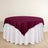 Round table with a burgundy tablecloth and white skirt.