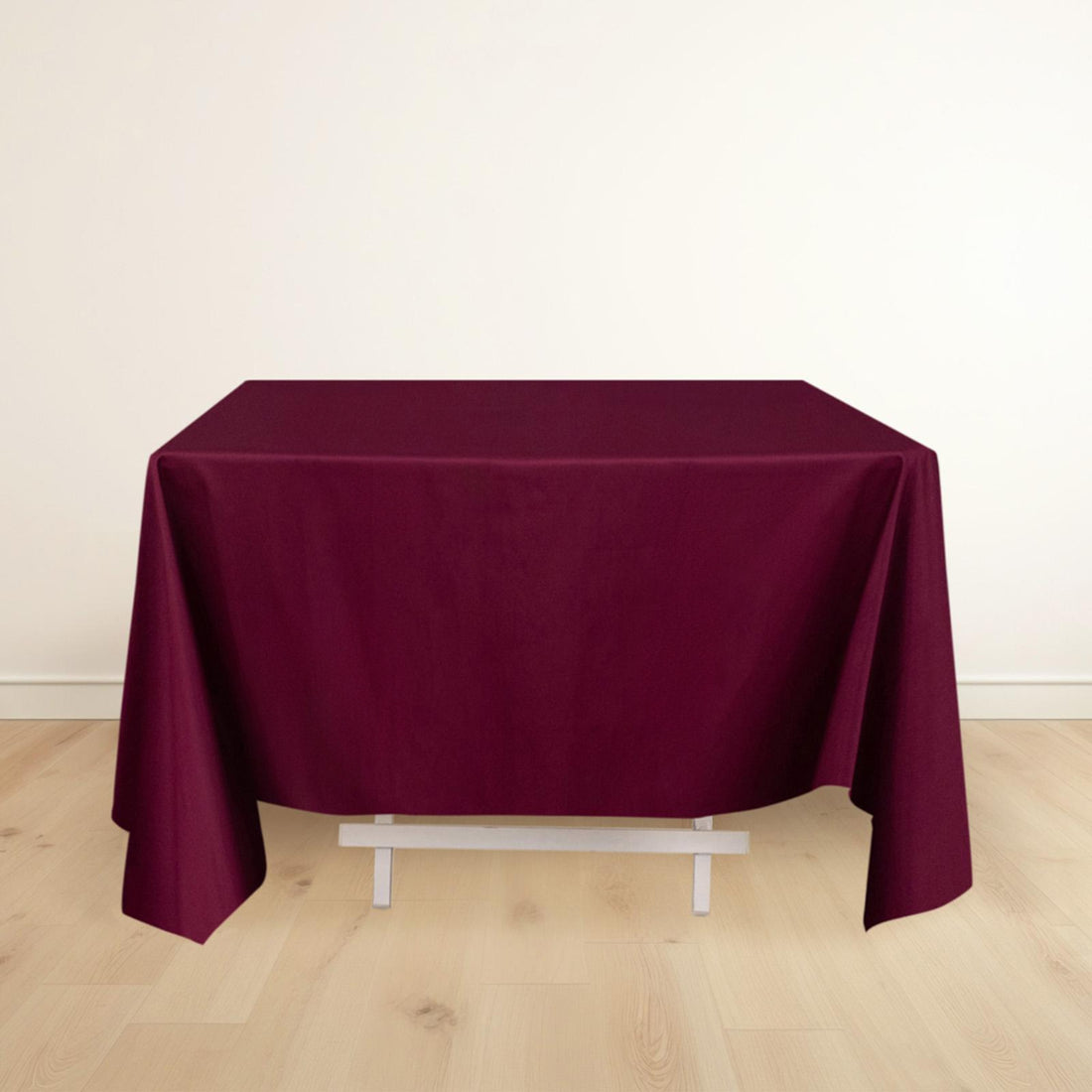 Burgundy tablecloth draped over a table on a light wooden floor.