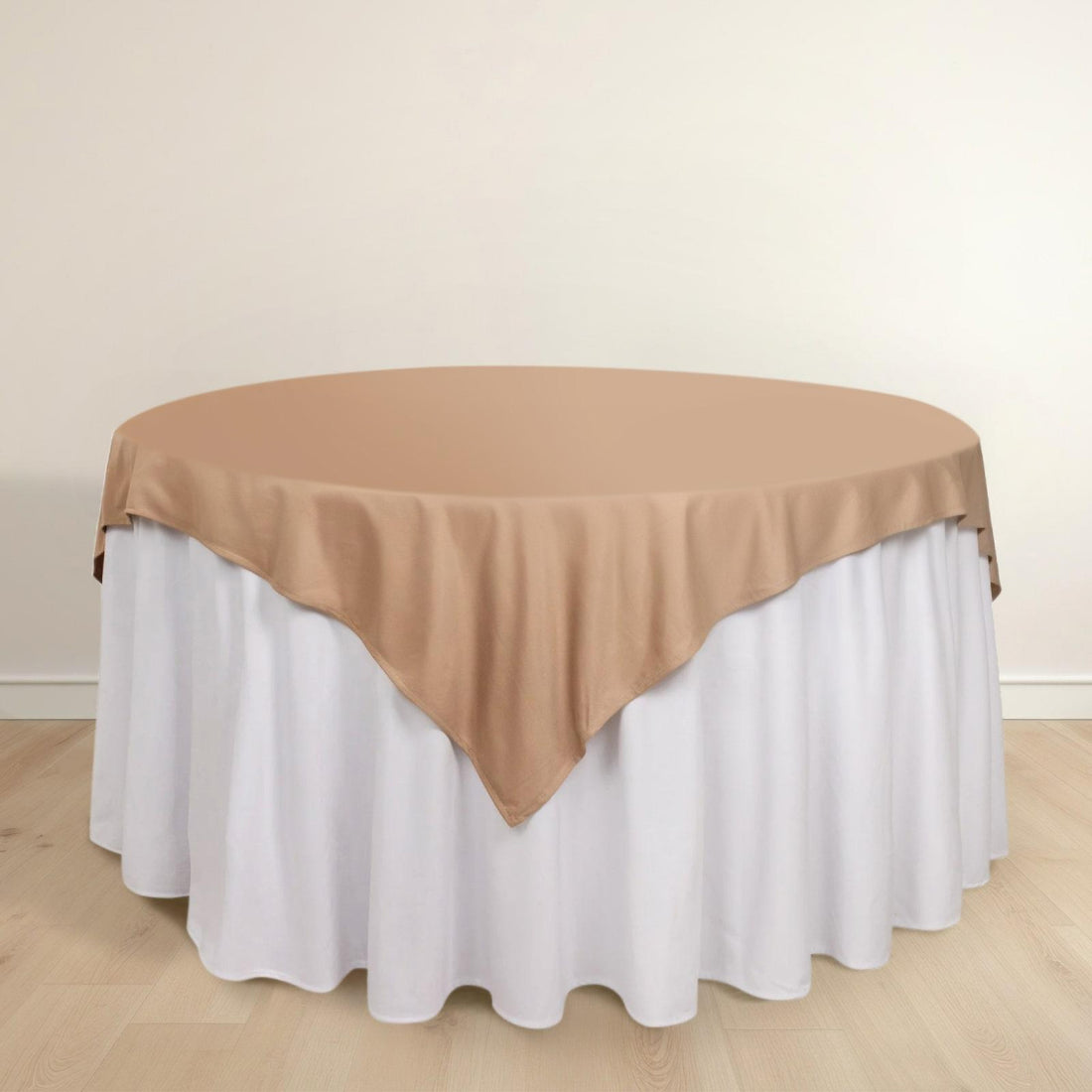 Round table with a beige cloth draped over a white table skirt.
