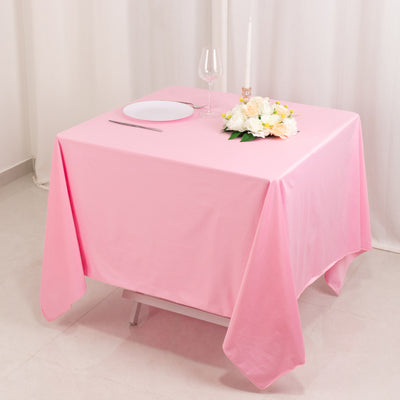 Pink tablecloth draped over a table set for dinner with flowers and a glass.