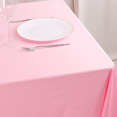Pink tablecloth with a white plate, fork, and wine glass set for dining.