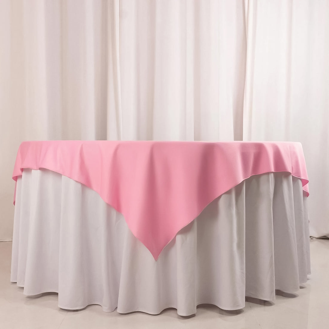 Pink tablecloth draped over a round table with white skirt.