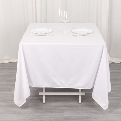 White tablecloth draped over a dining table with plates and glasses.