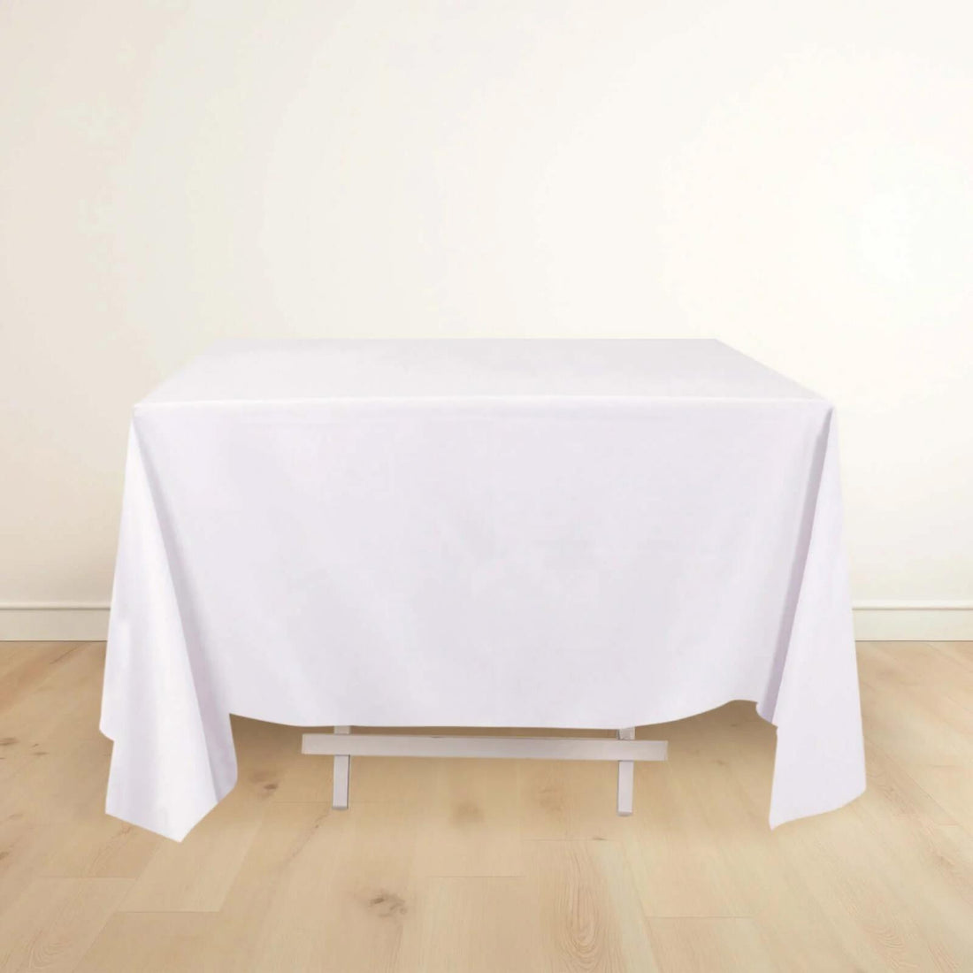 White tablecloth draping over a table on a light wooden floor.