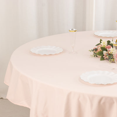 Round table set with white plates and floral arrangement on soft pink tablecloth.