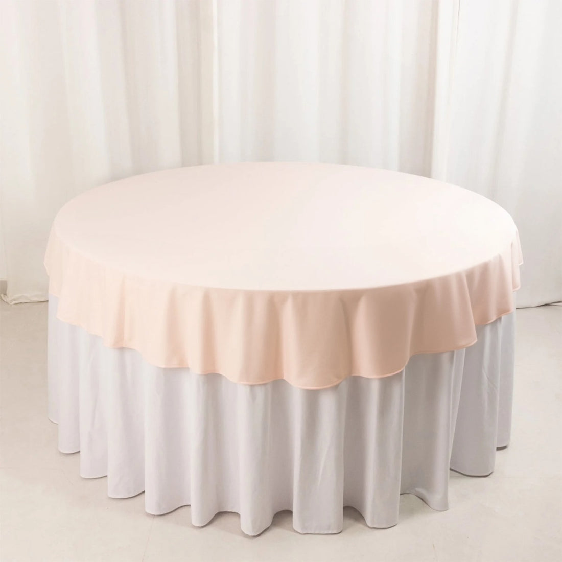 Round table covered with a soft pink tablecloth on a white table skirt