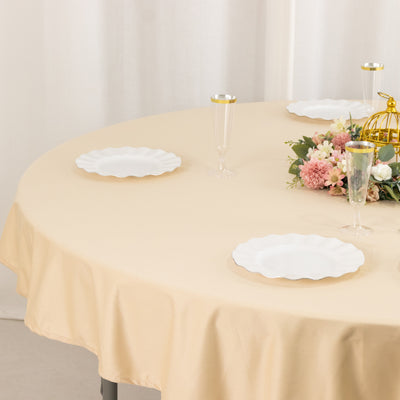 Elegant round table set with beige tablecloth, white plates, and floral centerpiece.