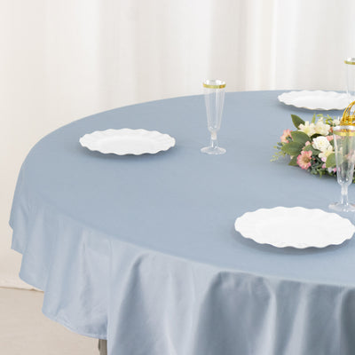 Round table set with blue tablecloth and white plates, adorned with flowers.