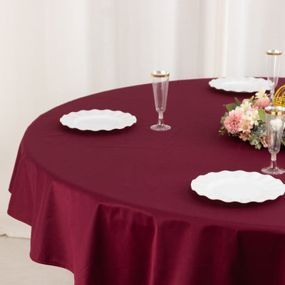 Burgundy tablecloth with white plates and floral centerpiece on a round table.