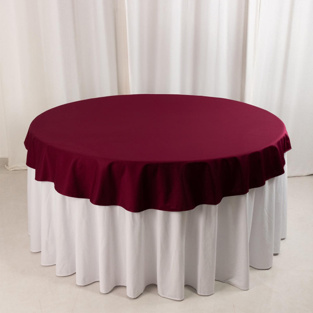 Burgundy tablecloth draped over a round table with a white skirt
