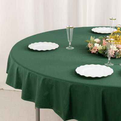 Green tablecloth on a round table set with white plates and floral centerpiece.