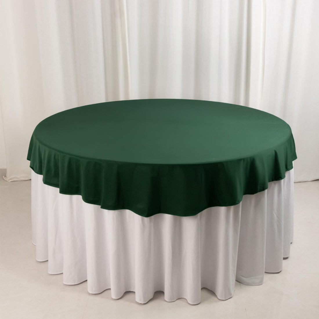 Green round tablecloth with white skirt on a plain backdrop.