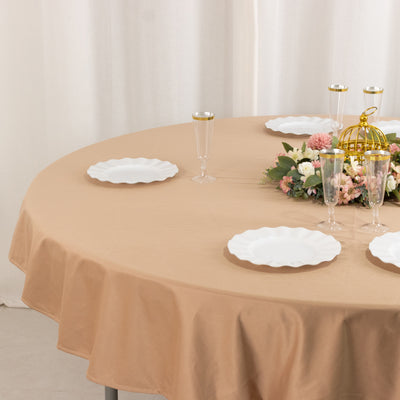 Round beige tablecloth set with white plates and floral centerpiece.