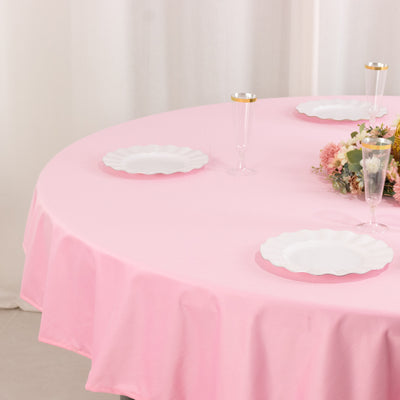 Pink tablecloth with white plates and floral centerpiece on a round table.