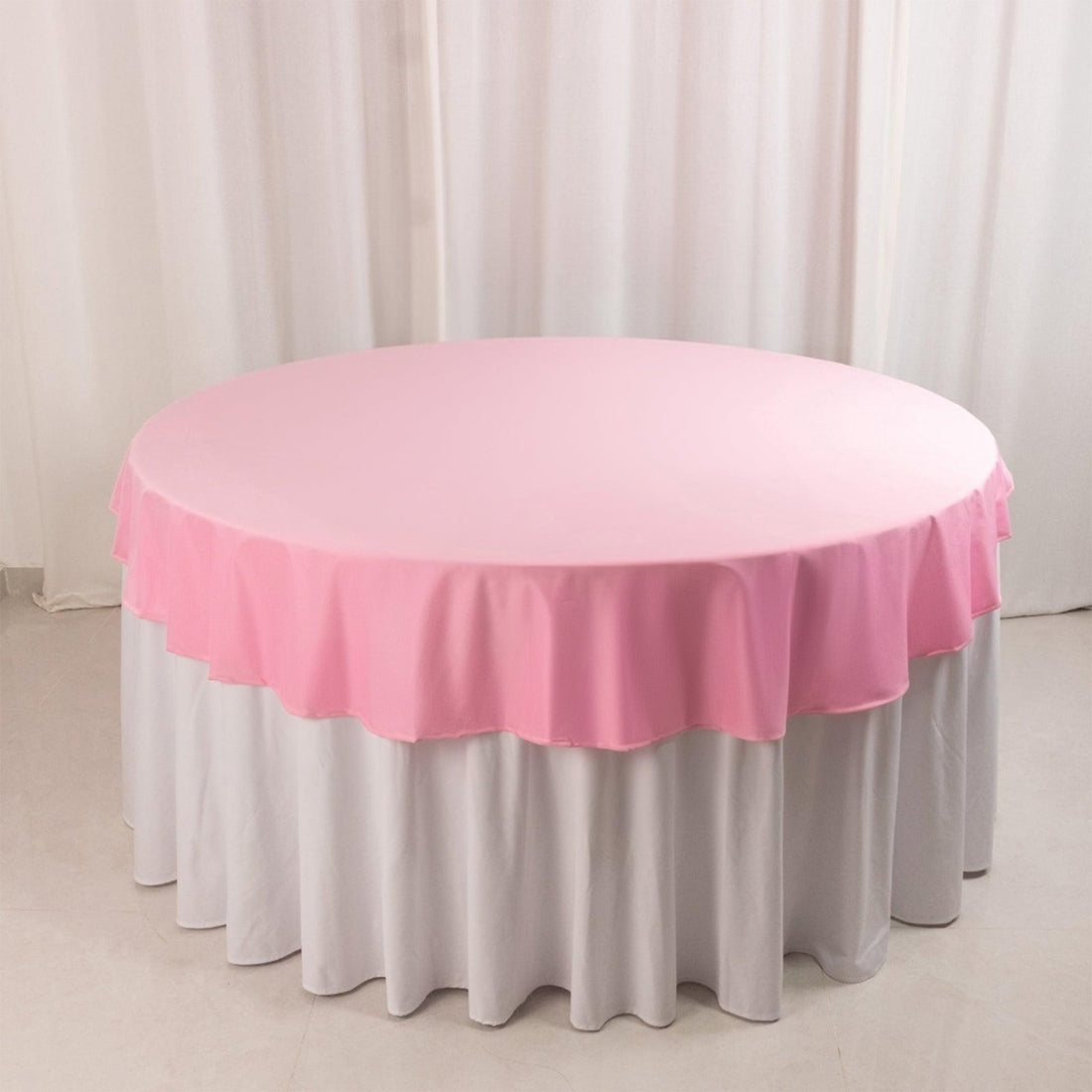 Round table with a pink tablecloth and white skirt.