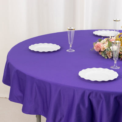 Purple tablecloth on a round table set with white plates and floral centerpiece.