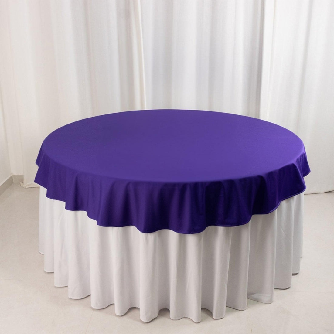 Purple round tablecloth with ruffled edges on a white table.