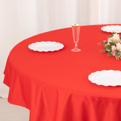 Red round tablecloth with white plates and floral centerpiece.
