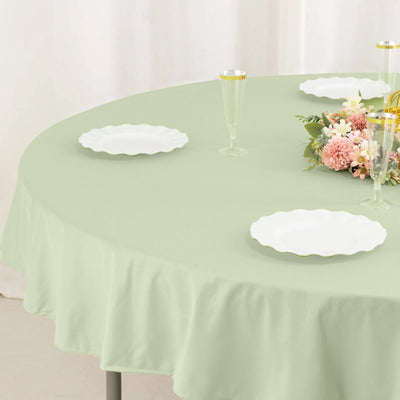 Round mint green tablecloth on a dining table with plates and floral centerpiece.