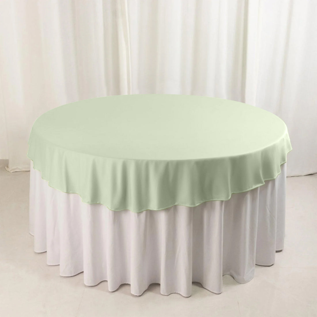 Round mint green table cover on a white tablecloth.