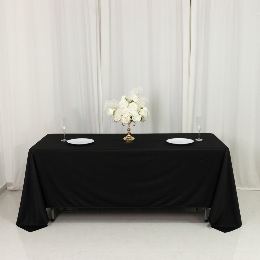 Elegant black table with floral centerpiece and plates set for dining.