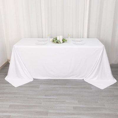White tablecloth draped over a table with plates and candles.