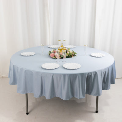 Round blue tablecloth with white plates and floral centerpiece on a round table.