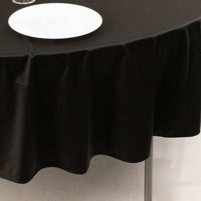 Black tablecloth draping over a round table with a white plate on top.