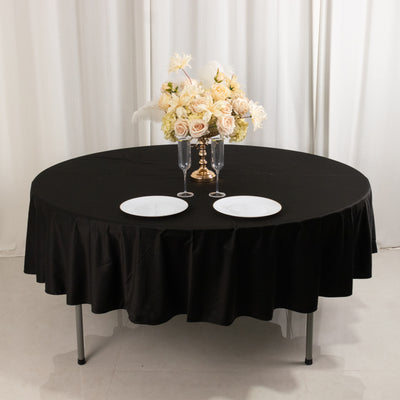 Round black table with a floral centerpiece and plates set for dining.