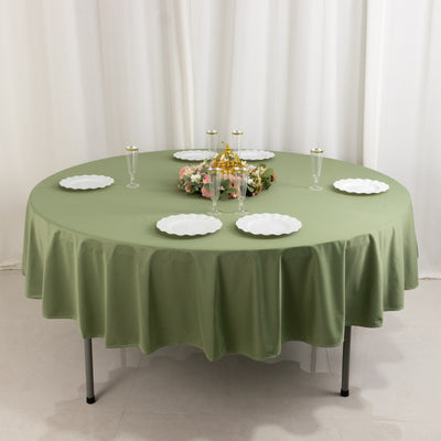 Round green tablecloth with white plates and floral centerpiece on a dining table.