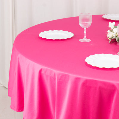 Pink tablecloth draped over a round table with white plates and a glass.