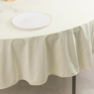 Round cream tablecloth draping over a table with a gold-rimmed plate.
