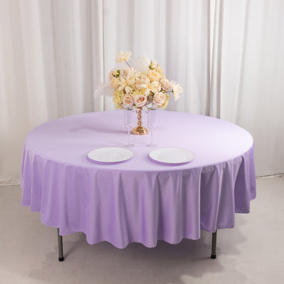 Round purple tablecloth with a bouquet of white roses and two plates on a table.