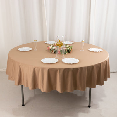 Round beige tablecloth draped over a table with plates and floral centerpiece.