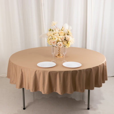 Round beige tablecloth with plates and floral centerpiece on a dining table.