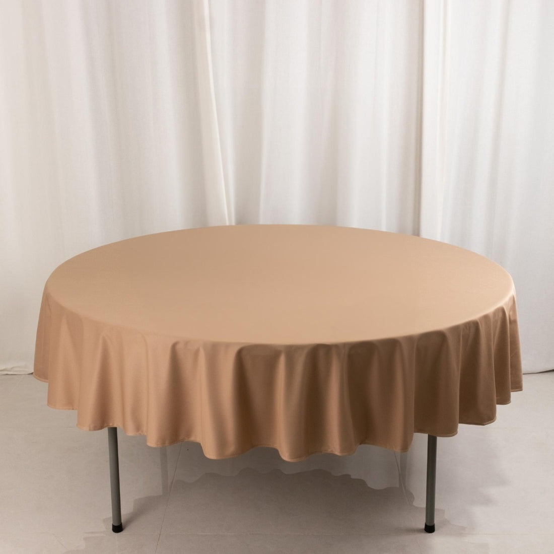 Round beige tablecloth on a circular table against a plain backdrop.