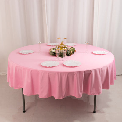 Round pink tablecloth draped over a table set with plates and floral centerpiece.